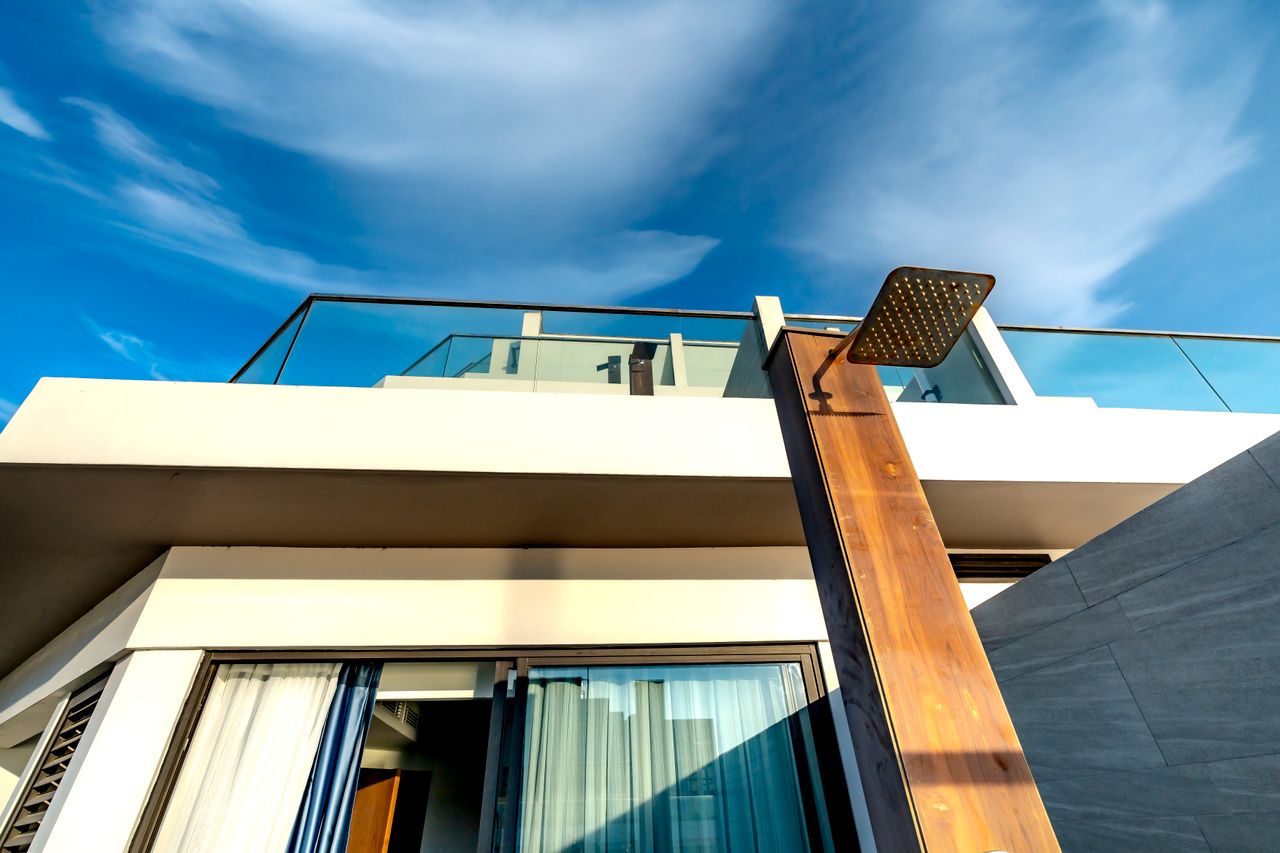 Services Contemporary terrace design with glass railings and outdoor shower against a vivid sky.